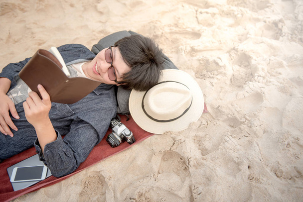 joven acostado en la playa de arena y leyendo su cuaderno
 - Foto, Imagen