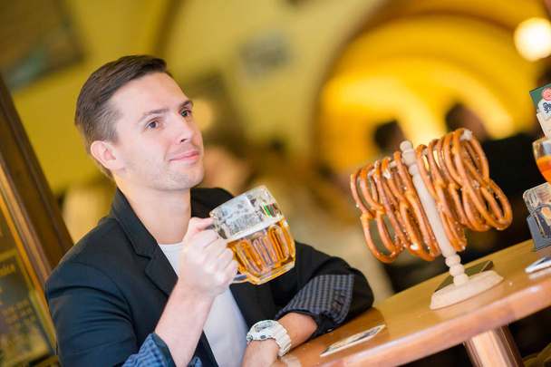 Молодий чоловік з пивом і солоними м'якими кренделями в бару для пива
 - Фото, зображення