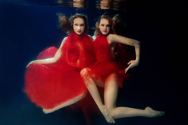 Podwodne portret ot dwie młode dziewczyny piękne z tworzą w czerwony stylowe sukienki pod wodą - Zdjęcie, obraz
