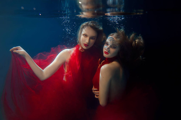 Underwater portrait ot two young beautiful girls with make up in red stylish dresses underwater - Photo, Image