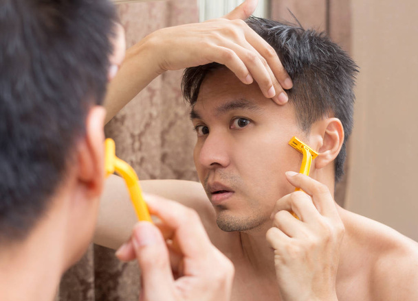 Mirror reflection of a young asian handsome man shaving - Фото, изображение