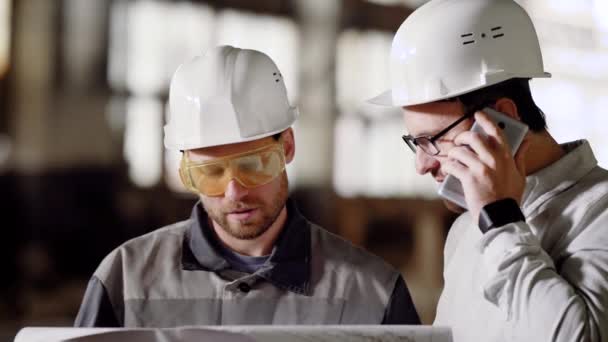 The foreman and architect in protective helmets call the customer on the mobile phone to the project customer to make changes in the construction plan - Footage, Video