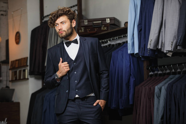 Modern young handsome businessman dressed in classical suit adjusting a tie while standing in the suit shop - 写真・画像