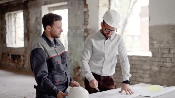 Podnikatel v helmu na hlavě a profesionální stavební projednávání plánů budovy, muži jsou na staveništi - Záběry, video