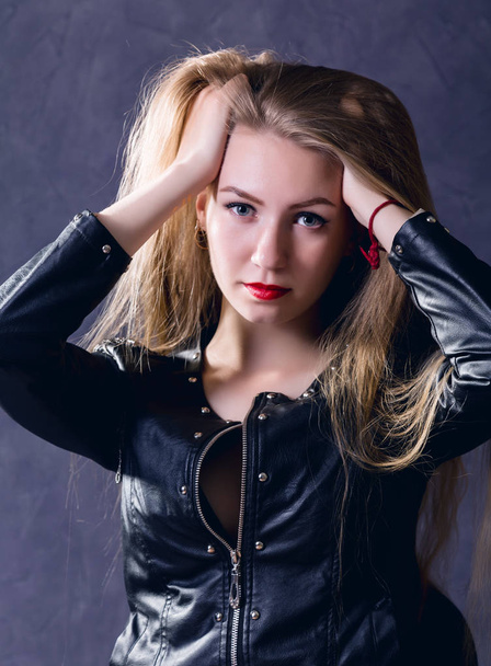 beautiful young woman in a leather jacket posing on a gray background - Photo, image