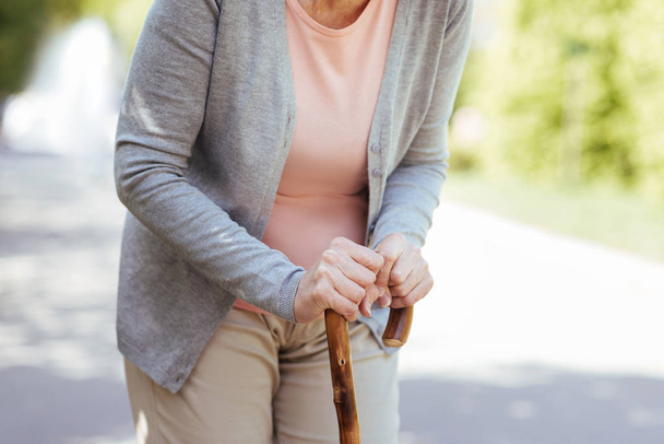 Aged woman leaning on the stick in the park - Photo, Image