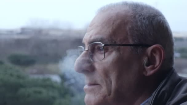 Thoughtful worried old  man smokes a cigarette on the balcony- steady cam - Filmagem, Vídeo