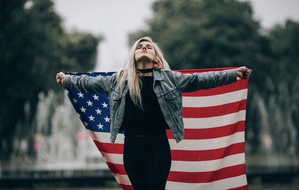 Młoda kobieta stoi i posiada amerykańską flagę. - Zdjęcie, obraz