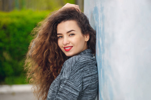 Portrait of an attractive young woman with curly hair standing with her back to the wall  - Foto, Imagem