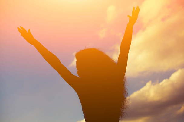Σιλουέτα του μια όμορφη κοπέλα που κρατώντας τα χέρια προς τις πλευρές κατά το φωτεινό ηλιοβασίλεμα - Φωτογραφία, εικόνα