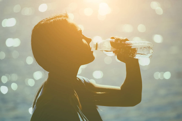 Silhouette d'une jeune athlète en survêtement buvant de l'eau d'une bouteille
  - Photo, image