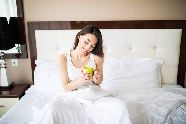 Bella donna che beve un caffè seduto sul suo letto a casa al mattino
 - Foto, immagini
