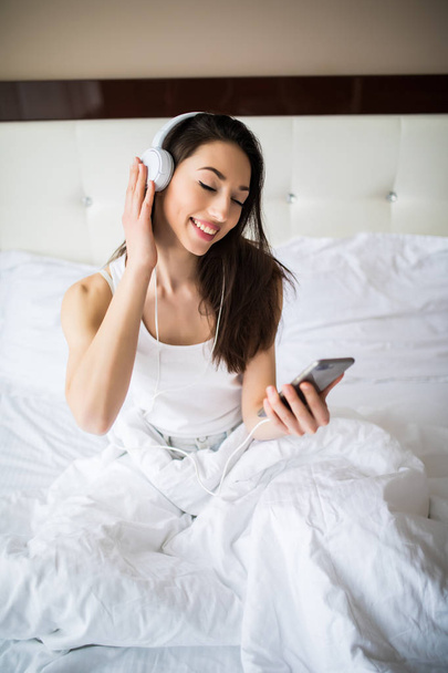 Happy woman or teenage girl in headphones listening to music from smartphone and dancing on bed at home - Fotoğraf, Görsel