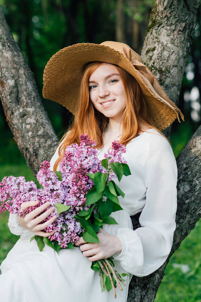 Redhead girl with a bouquet of lilacs in a spring garden - Foto, Imagen