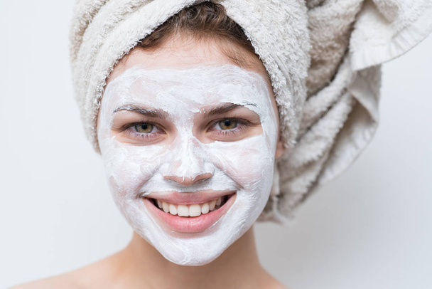 mooie vrouw na douche met een handdoek op haar hoofd en crème op gezicht. - Foto, afbeelding