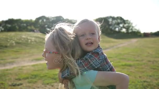 Siostra szczęśliwy przewożących cute little brother na plecach - Materiał filmowy, wideo