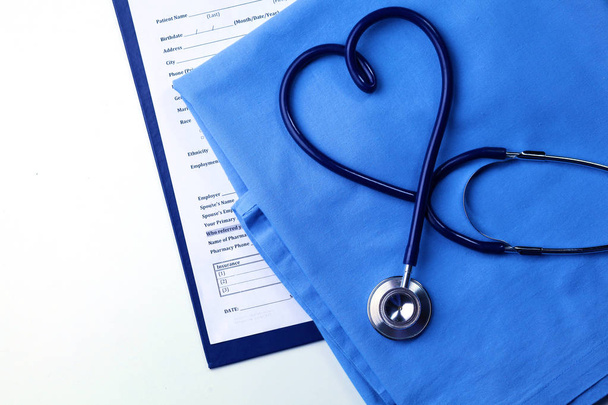 Ιατρικό στηθοσκόπιο στριμμένο σε σχήμα καρδιάς, που βρίσκεται στη λίστα του ιατρικού ιστορικού των ασθενών και ομοιόμορφη closeup μπλε γιατρός - Φωτογραφία, εικόνα