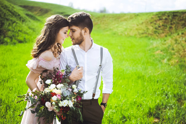 couple of a girl and  guy looking for a wedding dress, a pink dress flying with a wreath of flowers on her head on a background  garden and the blue sky, and they hug - Foto, imagen