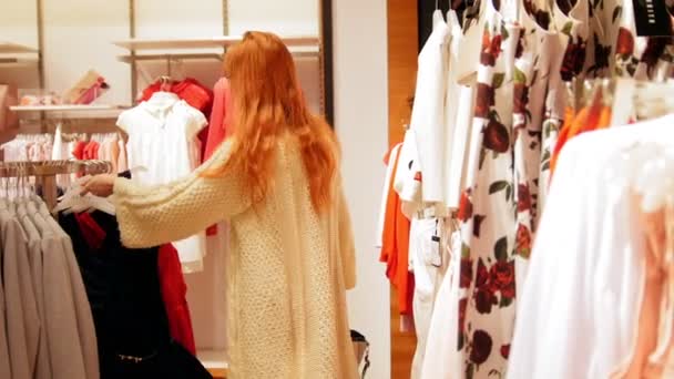 Γυναίκα ομορφιά σε ένα κατάστημα ιματισμού επέλεξε ένα φόρεμα - εμπορική έννοια - Πλάνα, βίντεο