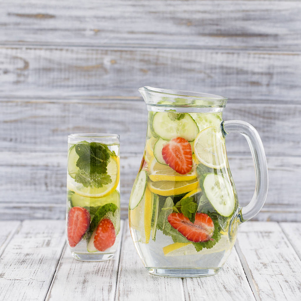 Dietary detox drink with lemon juice, red strawberry, cucumber and mint leaves in clear water with ice. - Foto, Bild