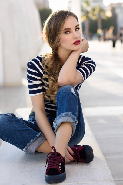 金髪の女性、ファッション、都市の背景に座ってのモデル. - 写真・画像