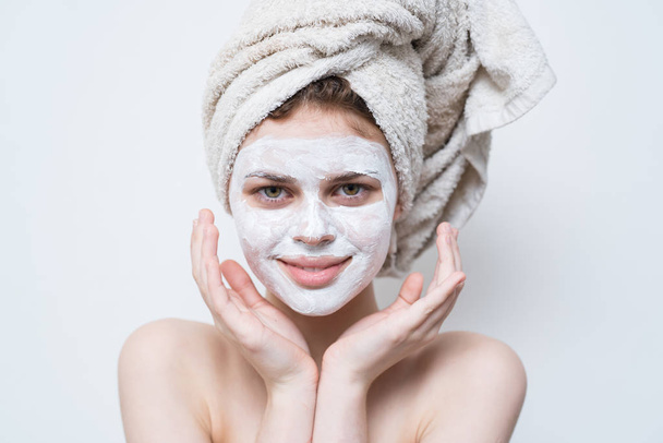 mooie vrouw na douche met een handdoek op haar hoofd en crème op gezicht. - Foto, afbeelding