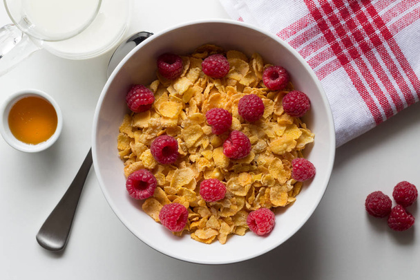 Breakfast cereal of cornflakes and raspberries, honey and milk o - Photo, Image