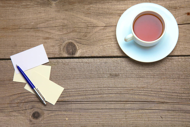 Tarjetas de visita en blanco con bolígrafo y taza de té en mesa de oficina de madera
 - Foto, imagen