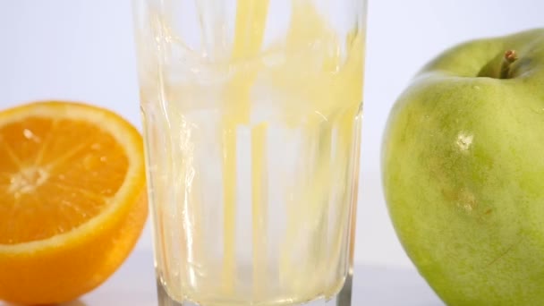 Orange and apple juice pouring in glass on color background - Filmagem, Vídeo
