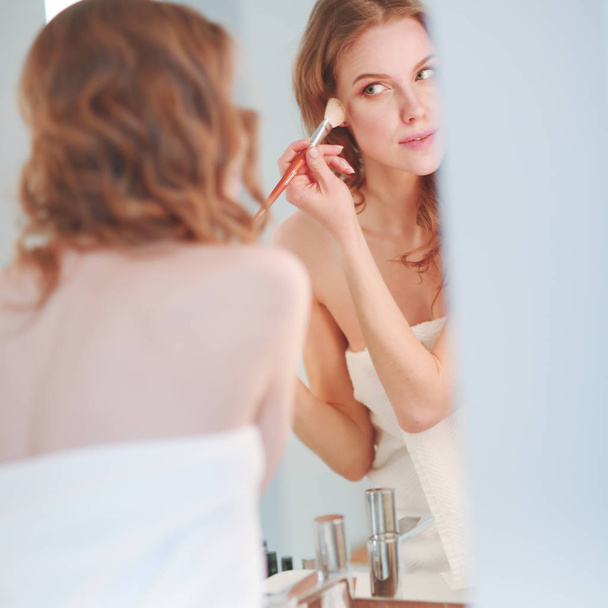 Young woman looking in the mirror and putting make-up on - Foto, Imagen