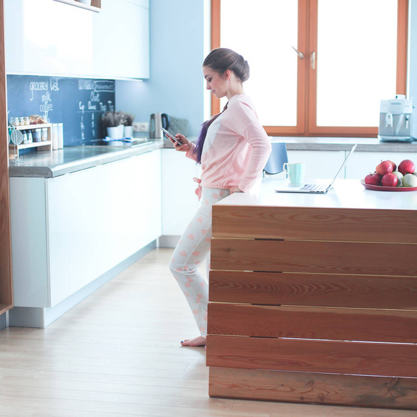 Woman using mobile phone standing in modern kitchen - Foto, Bild