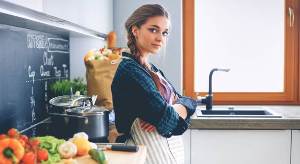 Young woman standing by the stove in the kitchen - Fotoğraf, Görsel