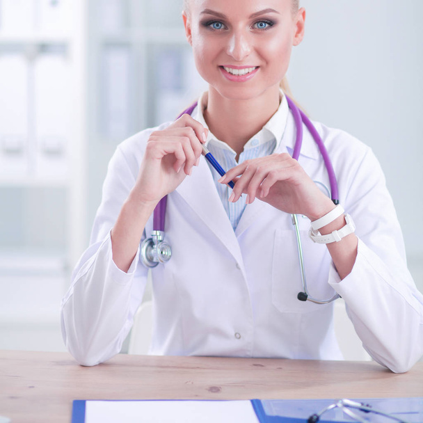 Beautiful young smiling female doctor sitting at the desk and writing. - Photo, Image