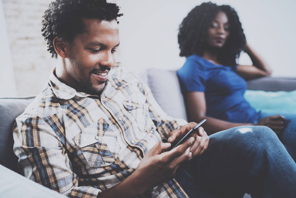 Smiling african american couple relaxing together on the sofa.Young black man using smartphones while rest at home in the living room. Horizontal,blurred background. - Foto, imagen