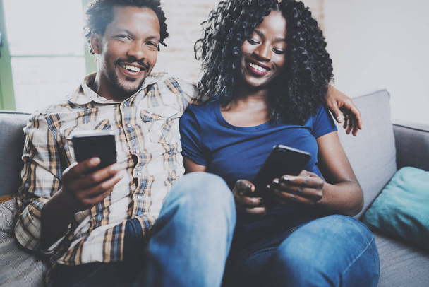 Happy african american couple relaxing together on the sofa.Young black man and his girlfriend using mobile phones while rest at home in the living room.Horizontal,blurred background. - Foto, imagen