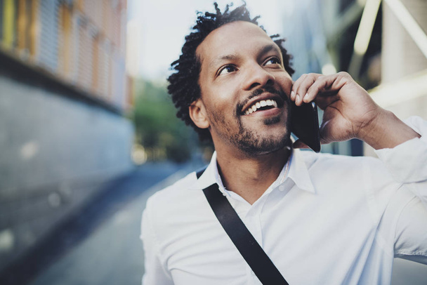 Portrait of happy American African black man using mobile phone to call friends at sunny street.Concept of happy young people enjoying gadgets outside.Blurred background. - Foto, Bild