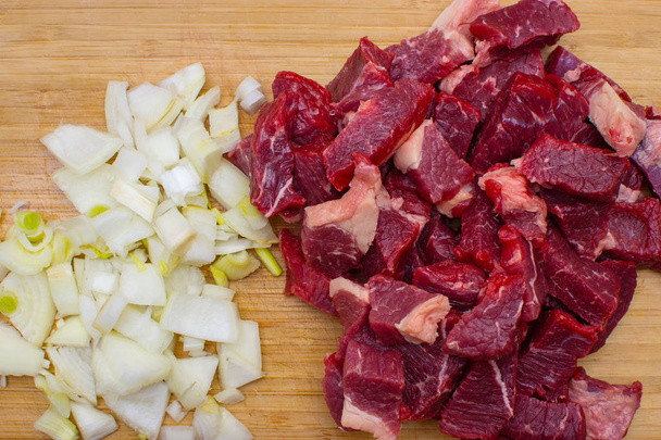 Čerstvé syrové maso nakrájené hovězí maso a nakrájenou bílou cibuli na dřevěném prkénku. - Fotografie, Obrázek