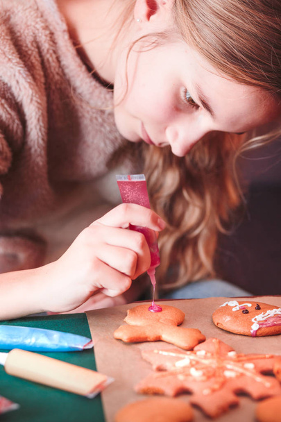 Girl decorating baked Christmas gingerbread cookies with frostin - 写真・画像