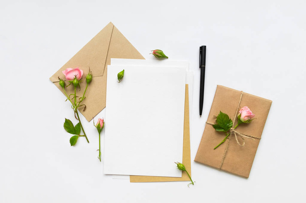Letter, envelope and gift on white background. Invitation cards, or love letter with pink roses. Holiday concept, top view, flat lay - Photo, image