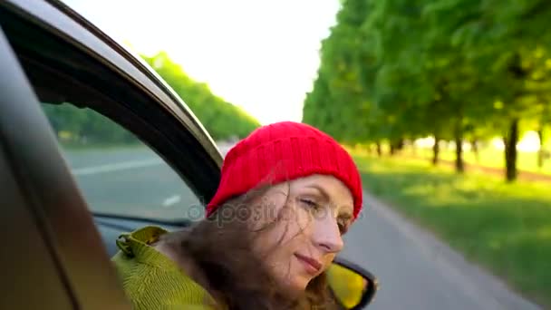 Gelukkig jonge vrouw in auto passagiersstoel zitten en kijkt uit raam op een zonnige dag - Video