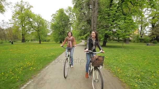 Front View of Two Female Friends Riding on Bicycles in the City Park in Spring. Camera in Motion. - 映像、動画