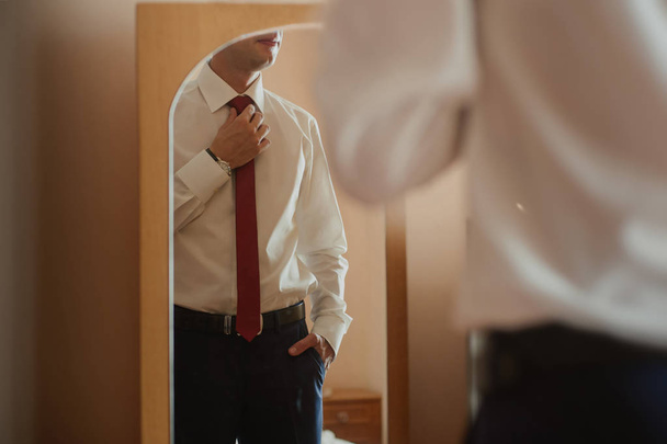 Liikemies valkoisessa paidassa ja solmiossa katsoo itseään peilistä.
 - Valokuva, kuva