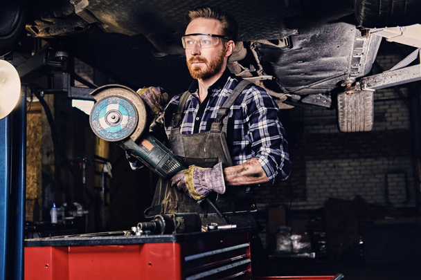 Mechanic in protective googles holds grinder - Photo, Image