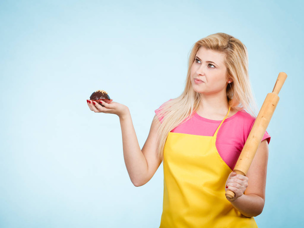 Woman holding cupcake and rolling pin wearing apron - Фото, зображення