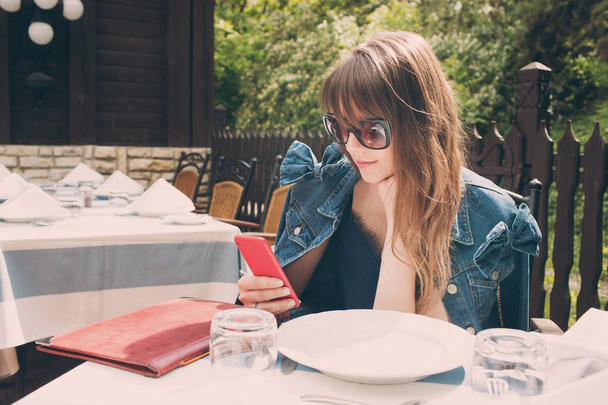 Una mujer sonriente en un restaurante con teléfono en las manos. espera para traer comida
 - Foto, Imagen