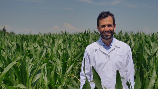Portrait of a farmer smiling at the camera, looking and checking the cornfield, greens background. Concept: ecology, corn, bio product, inspection, water, natural products, professional, environment. - 写真・画像