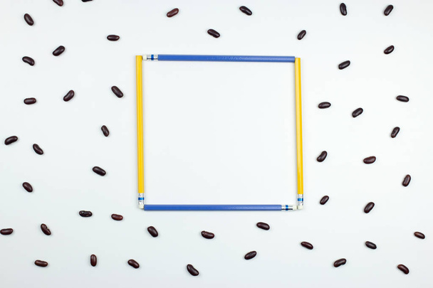 blue and yellow pencils frame with red beans on white background - Фото, зображення