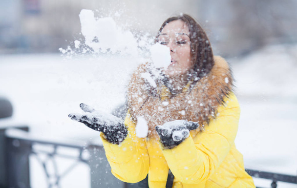 Happy beautiful young woman blowing snowflakes from her hands in a winter day - Foto, immagini