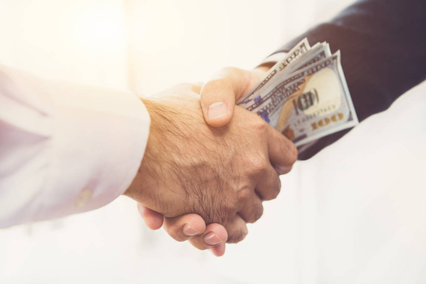 Бізнесмени роблять рукостискання з грошима в руках
  - Фото, зображення