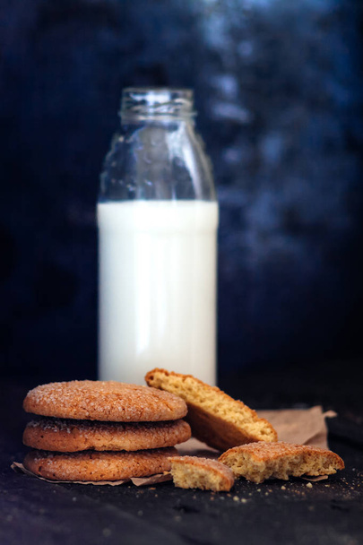 Garrafa com leite e uma pilha de biscoitos em um fundo escuro, re
 - Foto, Imagem